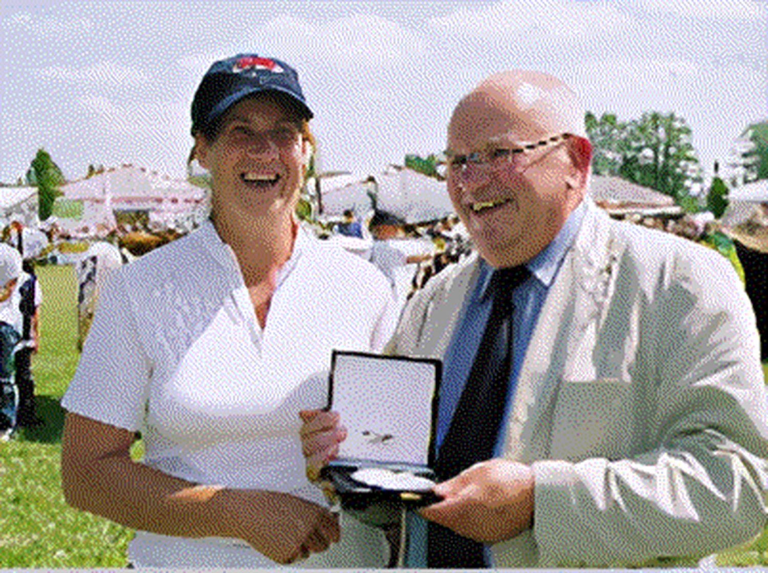 Bauer Zorn - Der Hofladen - Dieses Bild zeigt eine Frau in weißem Hemd und Mütze, lächelnd neben einem älteren Mann im Anzug, der ihr in einer Schachtel eine Medaille überreicht.